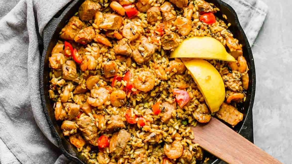 Shrimp and rice in a skillet with a lemon wedge.
