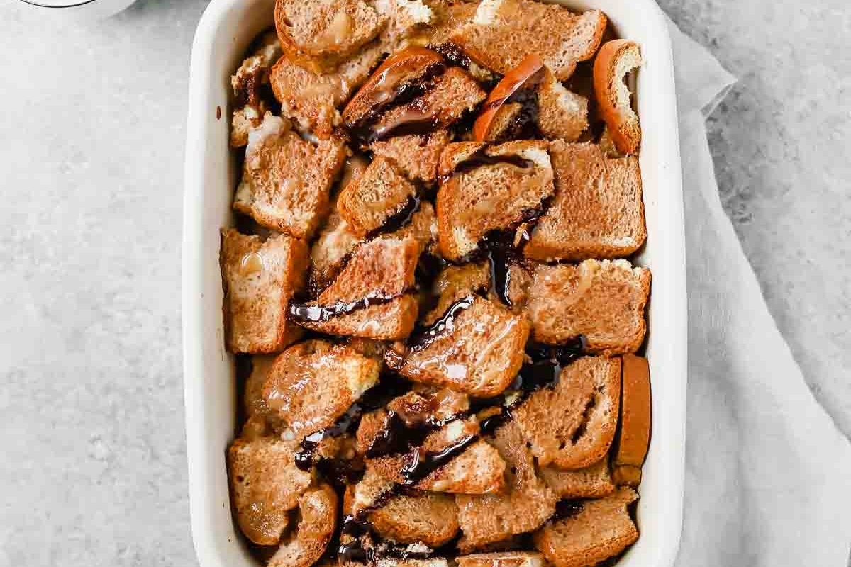 Christmas bread pudding bakes in a white dish with chocolate sauce.