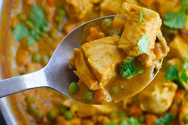A spoon full of chicken curry in a pan, perfect for curry enthusiasts looking for new recipes.