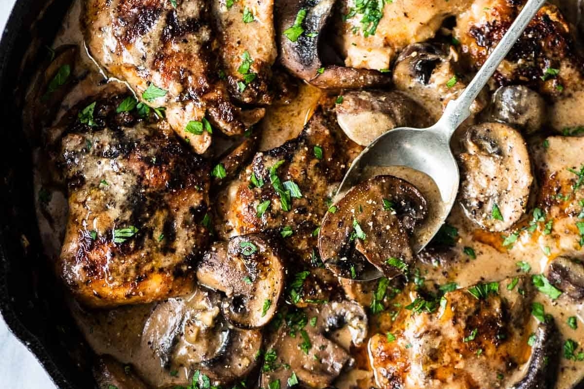 Chicken thighs with mushrooms and sauce in a skillet.