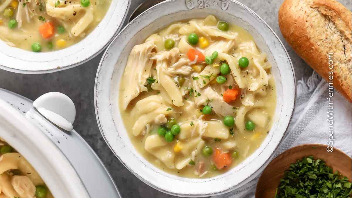 A hearty bowl of slow cooker chicken noodle soup loaded with tender chunks of chicken, vibrant carrots, and peas.