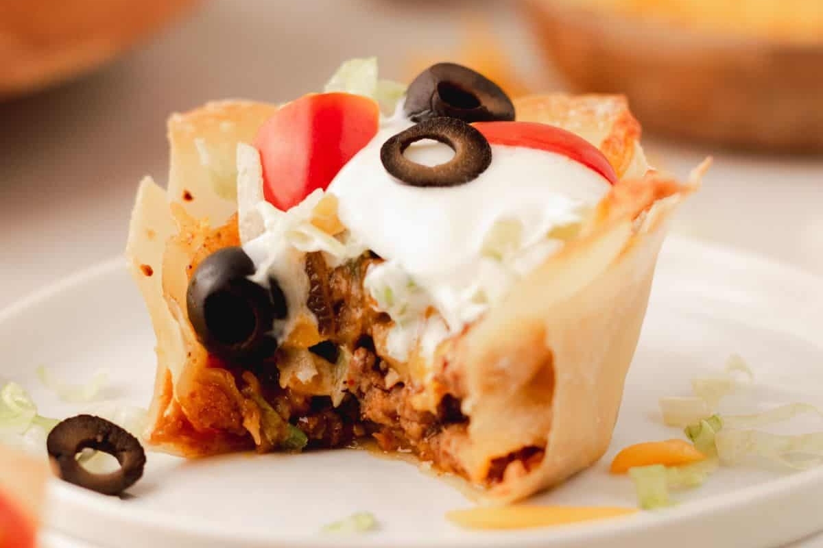 48 Easy Bite-Sized Appetizers Party Guests Will Love 24 Bite-sized Mexican taco cups, perfect for game day, topped with sour cream and olives on a plate.