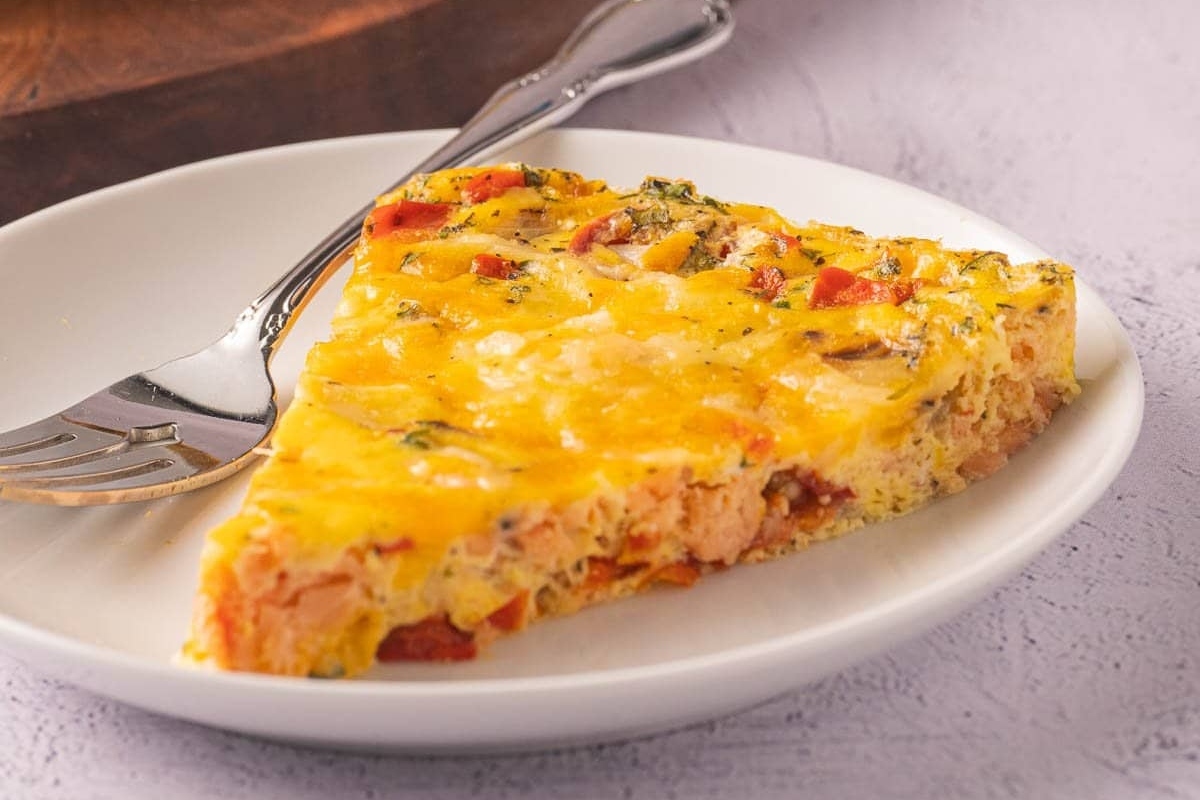 A healthy slice of salmon quiche with high protein on a plate with a fork.