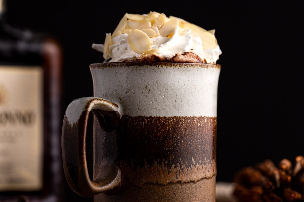 A mug of cocoa filled with fluffy whipped cream and a bottle of gin.