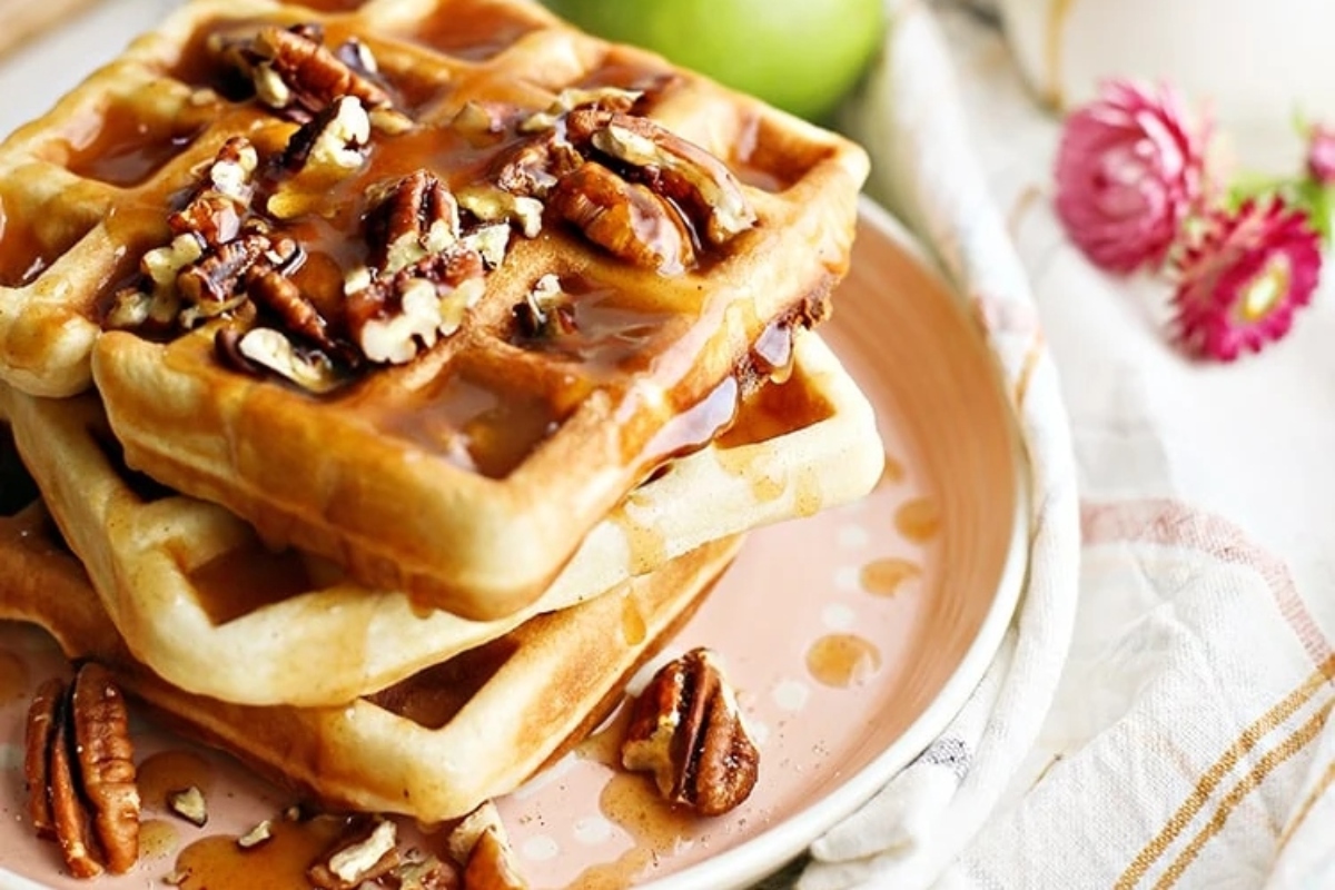 A stack of waffles with pecans and syrup on a plate, perfect for indulging in delicious waffle recipes.