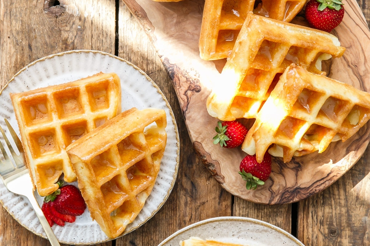 Delicious waffles topped with fresh strawberries and drizzled with syrup on a rustic wooden table.