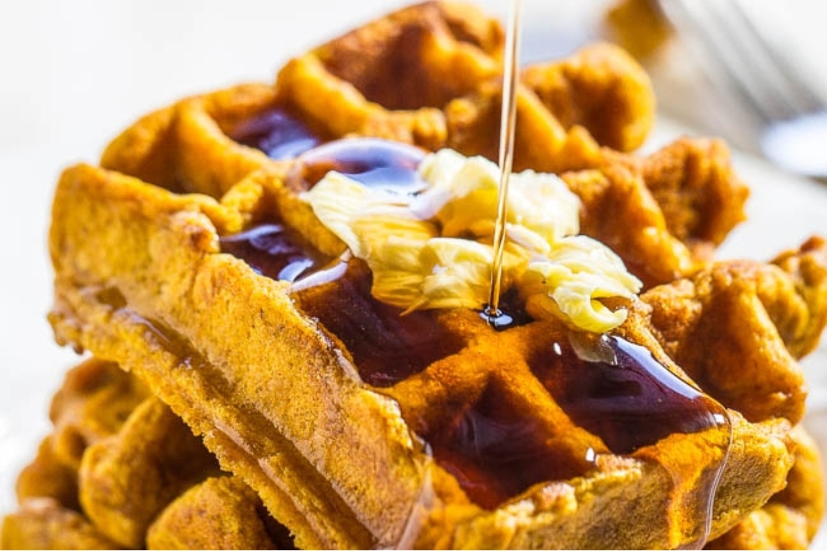 A stack of pumpkin waffles being drizzled with syrup, perfect for your next brunch gathering.