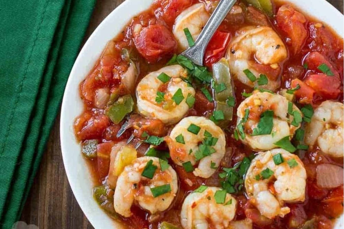        Recipe for shrimp stew served in a white bowl with a spoon.