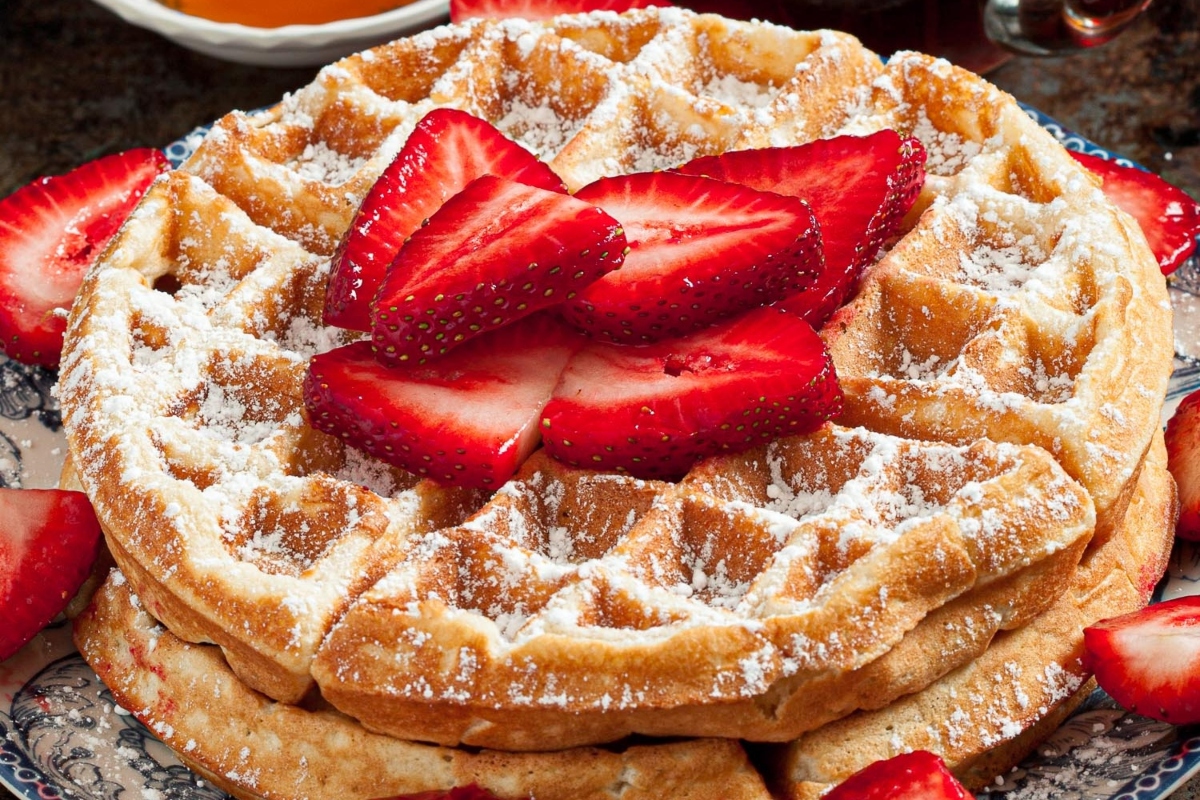 Delicious waffles topped with fresh strawberries and a dusting of powdered sugar, served on a plate.