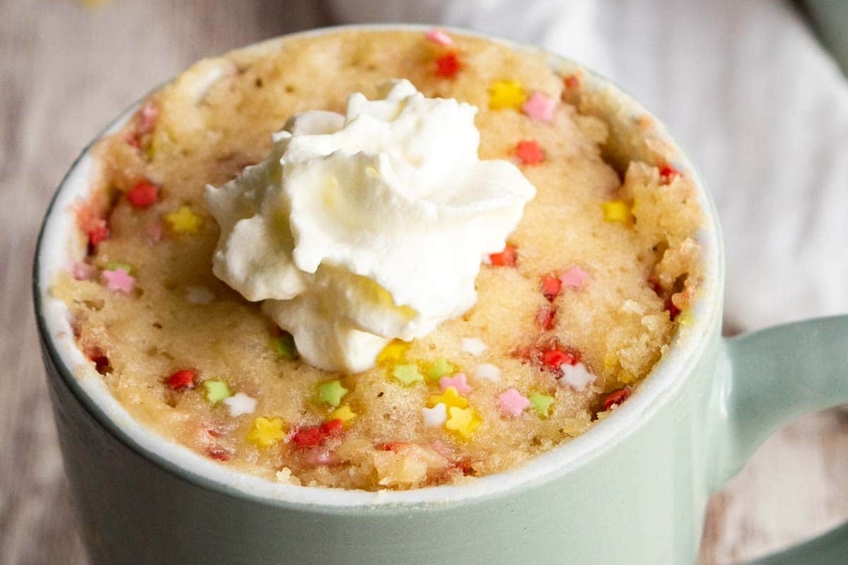 A delectable mug cake adorned with whipped cream and sprinkles.