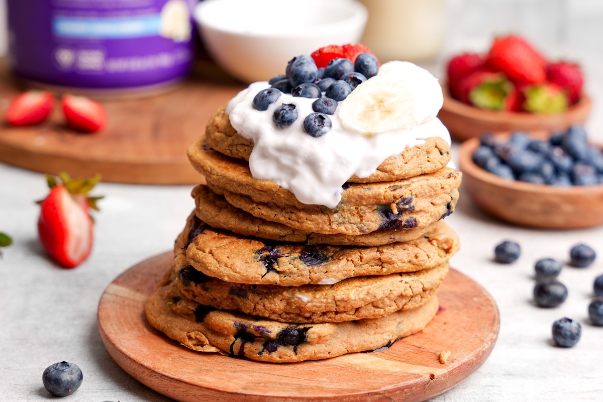 A stack of healthy blueberry pancakes with whipped cream and strawberries.