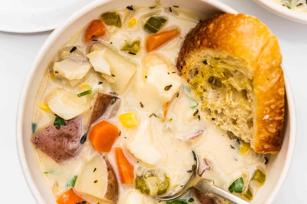 A bowl of chicken chowder with bread and vegetables, perfect for a satisfying and comforting soup.