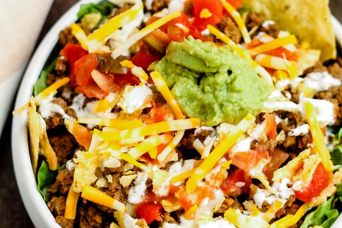 Enjoy a delicious bowl of taco salad, topped with creamy guacamole and tangy sour cream. Perfect for Taco Night dinners!