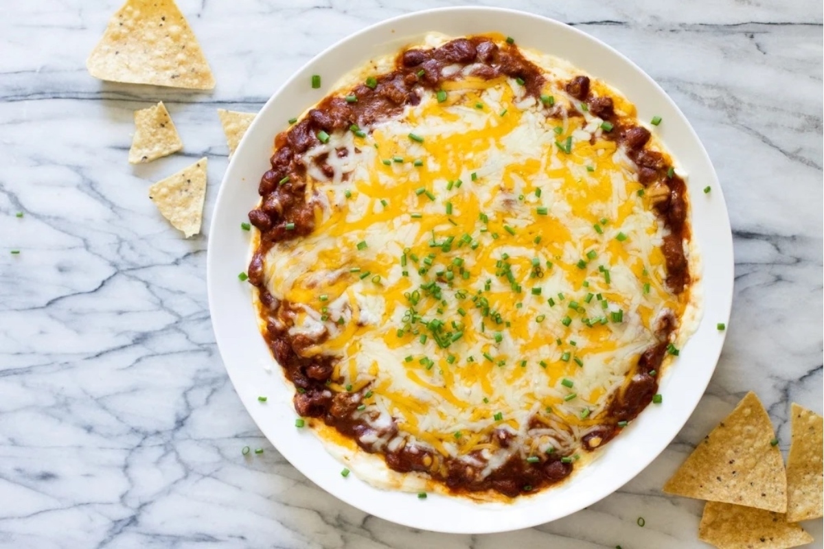 Creamy chili dip in a white bowl with tortilla chips.