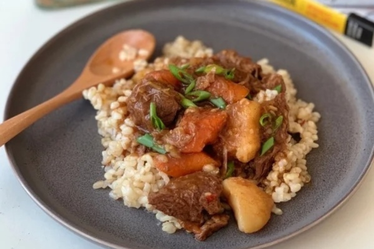 This dish is a classic example of a mouthwatering beef stew, served on a plate along with fluffy rice and accompanied by a trusty wooden spoon.