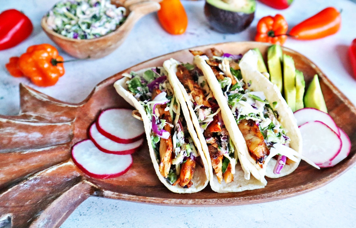 Jerk chicken tacos on a wooden plate with radishes.