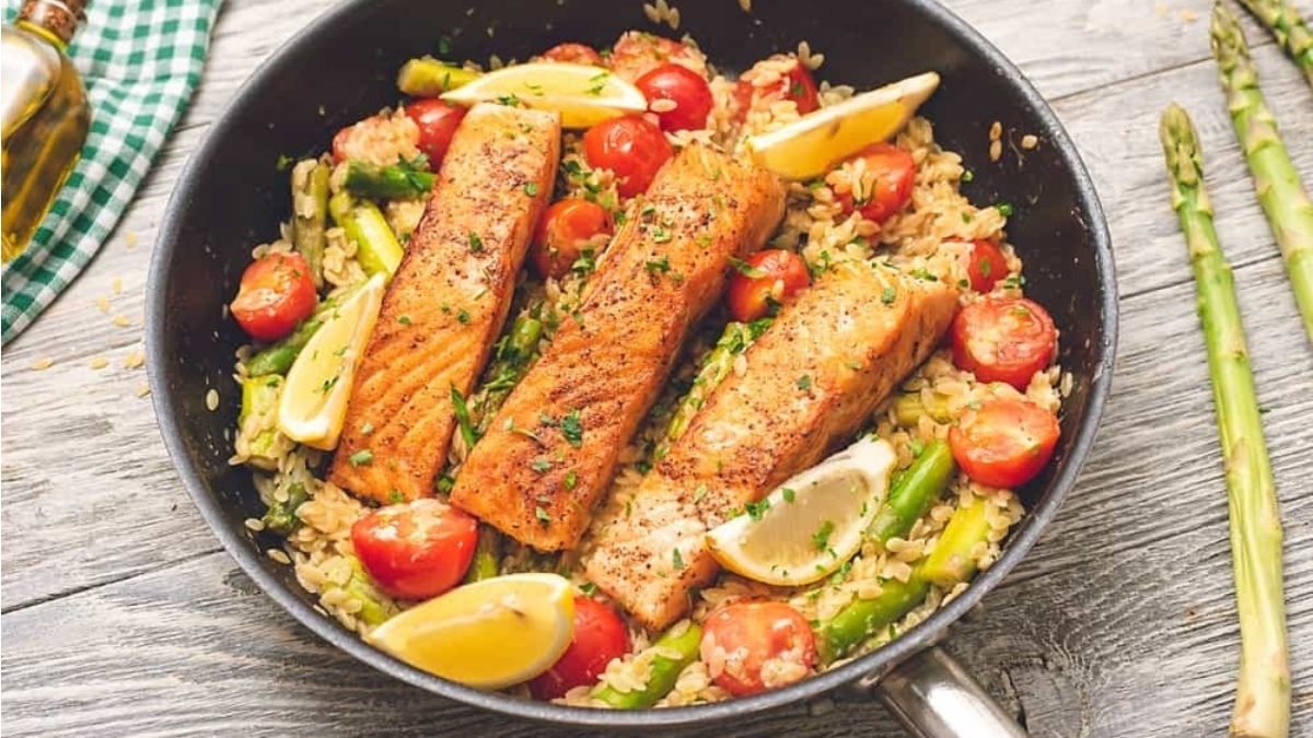 A romantic Valentine's Day main dish featuring salmon and asparagus sizzling in a skillet on a rustic wooden table.