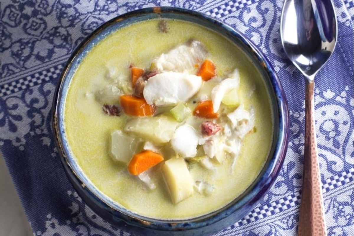 A bowl of Chowder soup with carrots, potatoes, and fish.