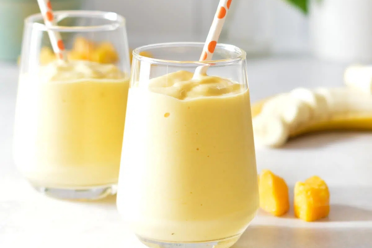 Two glasses of protein smoothie with bananas and straws.