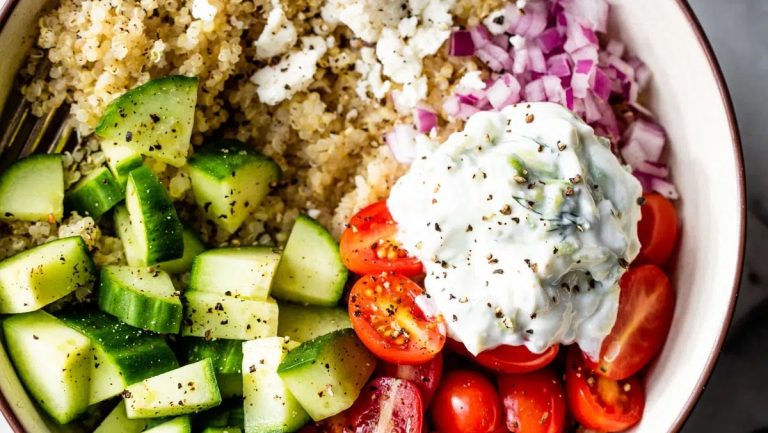 A grain bowl of quinoa salad with cucumbers, tomatoes, and sour cream.