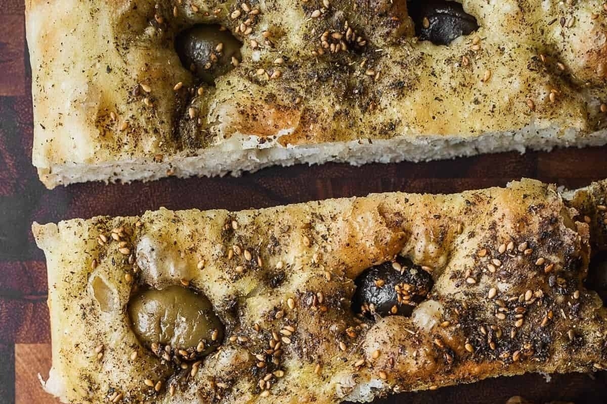 A mouthwatering recipe for focaccia, consisting of two slices of bread topped with olives and sesame seeds, beautifully presented on a cutting board.