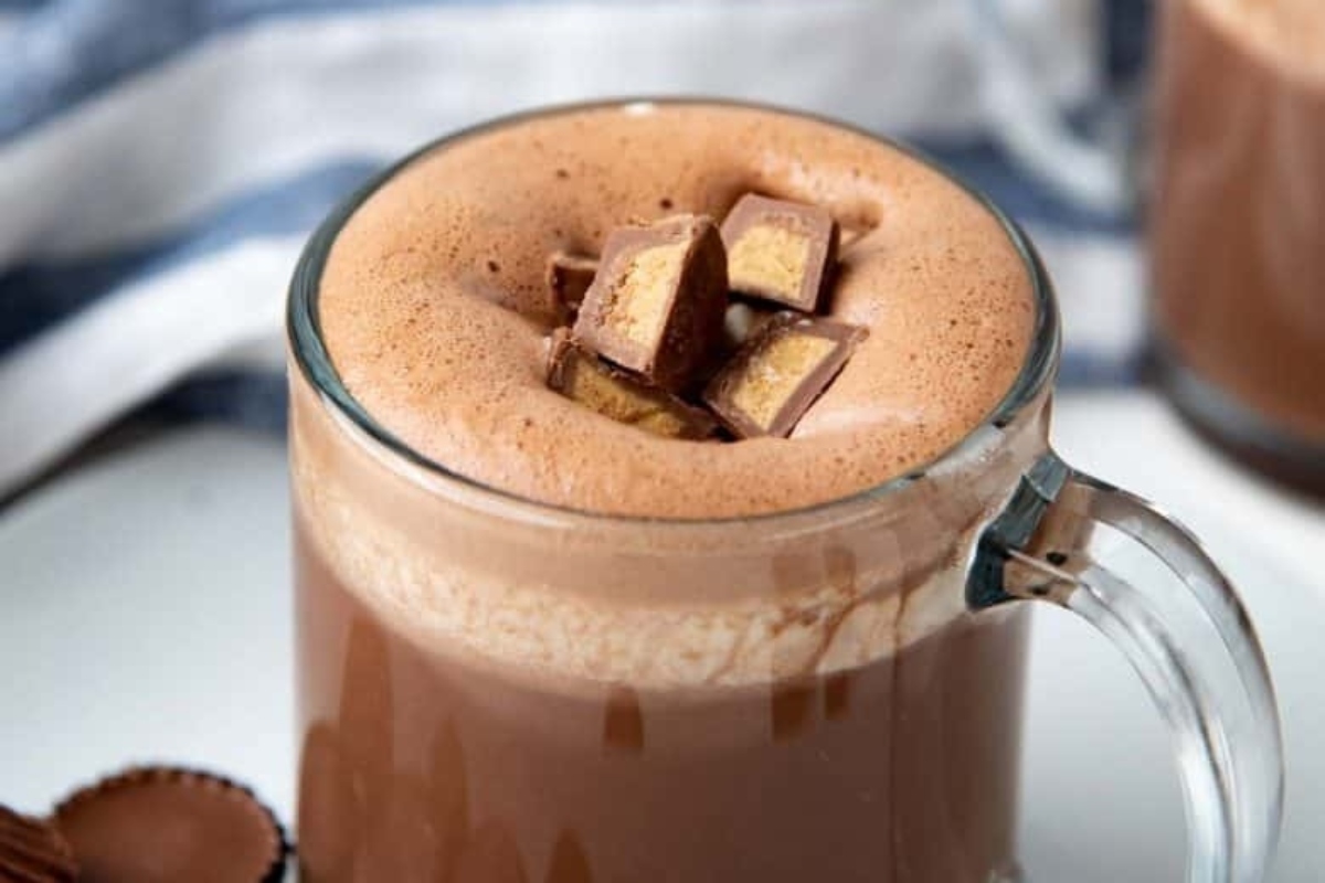 A steaming cup of cocoa with a peanut butter cup on top.