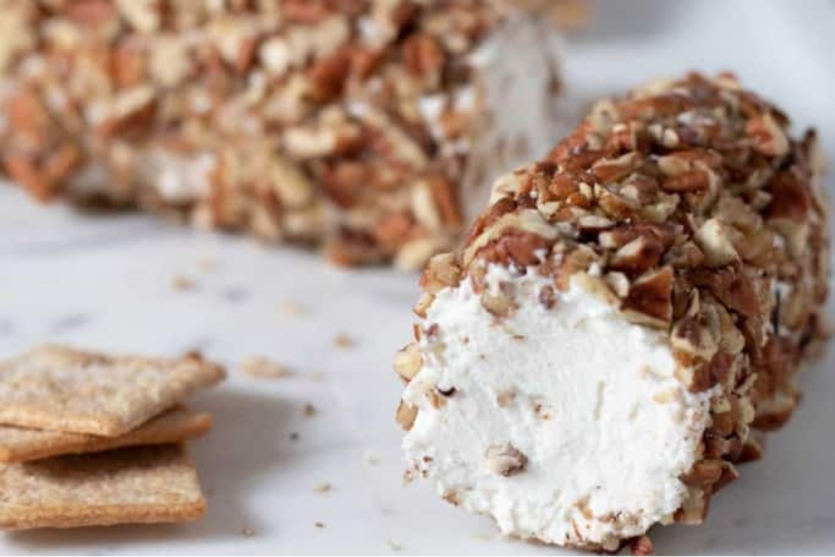 An appetizing goat cheese ball garnished with nuts and served alongside crackers on a clean white plate.
