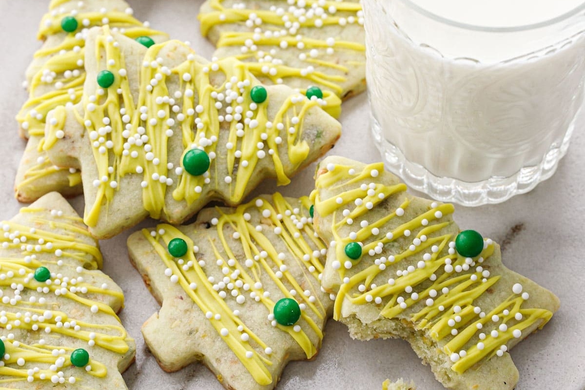 A plate of sugar cookies with green sprinkles and a glass of milk.