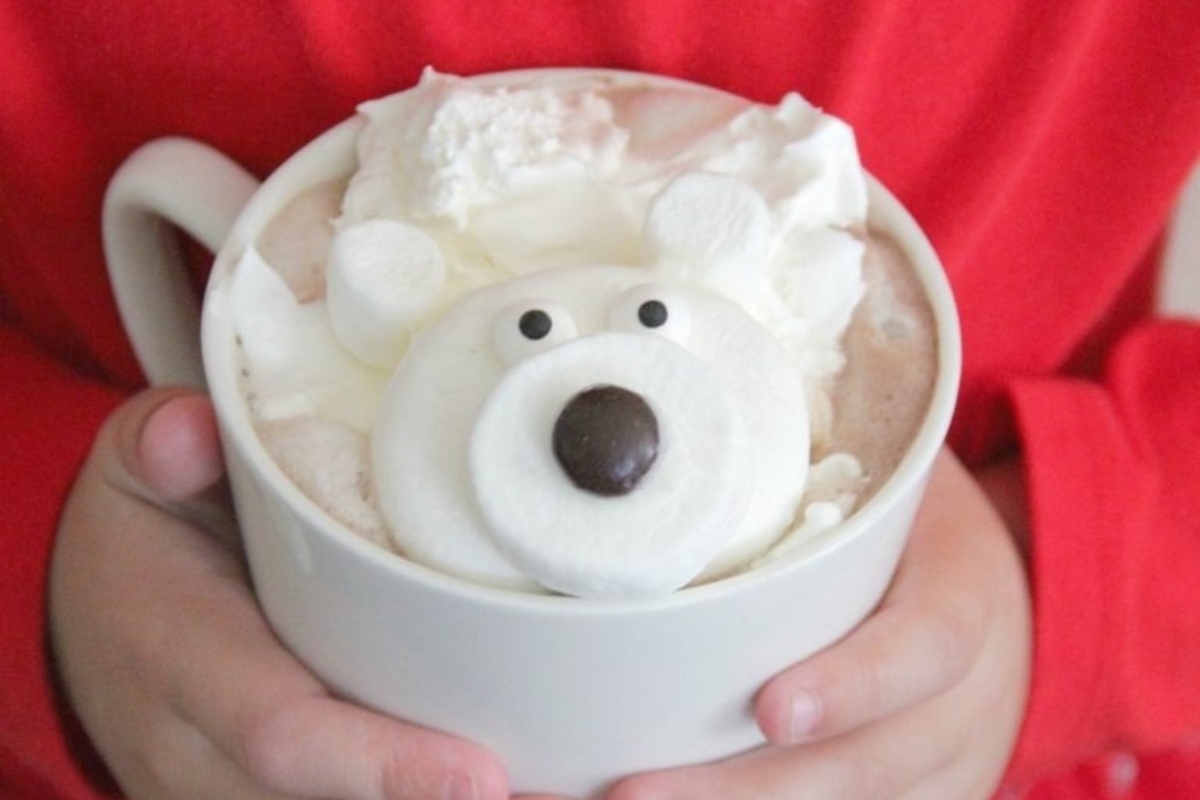 A child is embracing a cup of hot chocolate adorned with a polar bear.