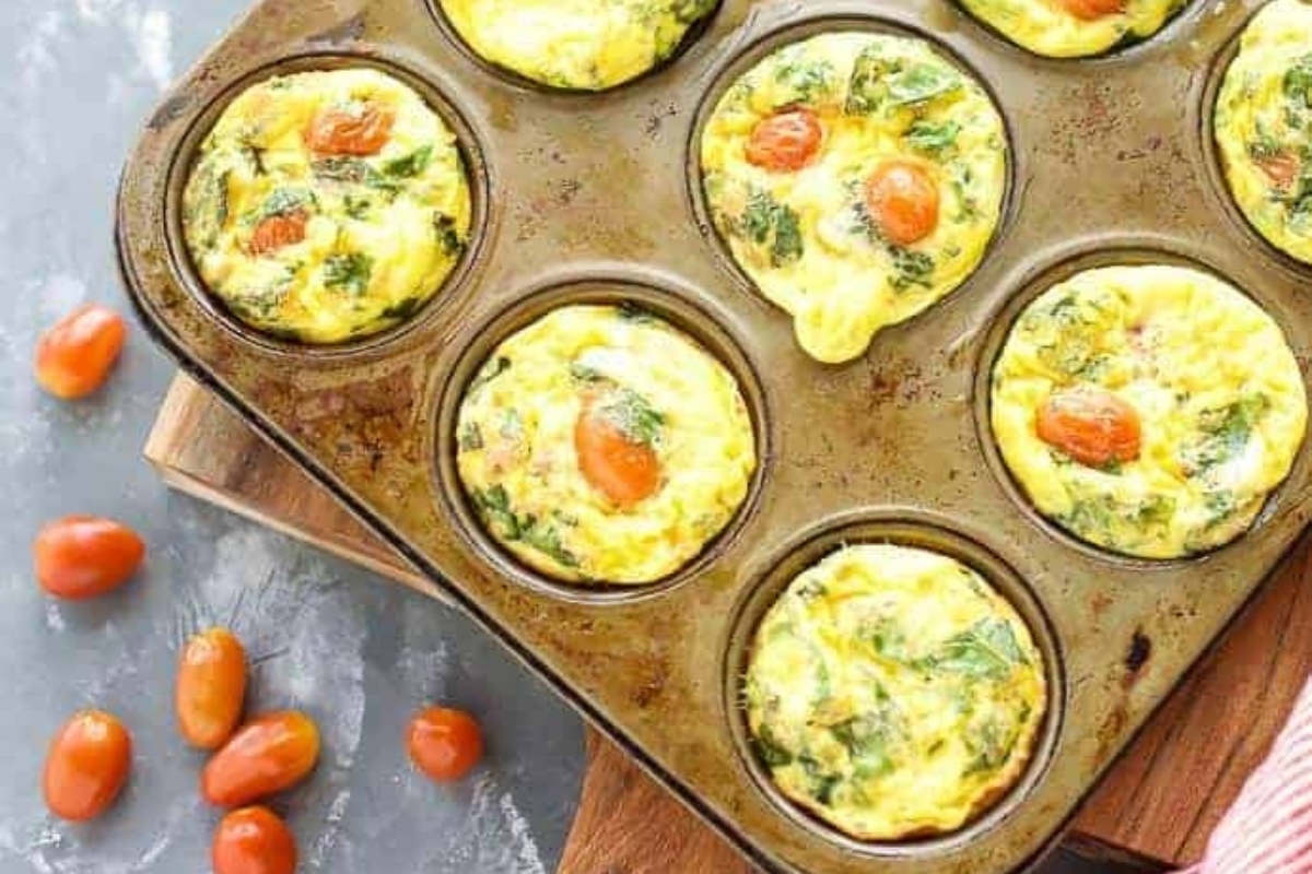 A healthy breakfast of high protein egg muffins, filled with spinach and tomatoes, baked in a muffin tin.