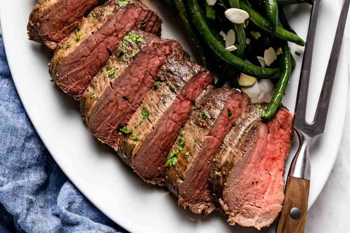 A succulent beef steak on a plate, perfectly paired with crisp green beans and accompanied by a gleaming fork. Perfect for Christmas dinners or any special occasion.