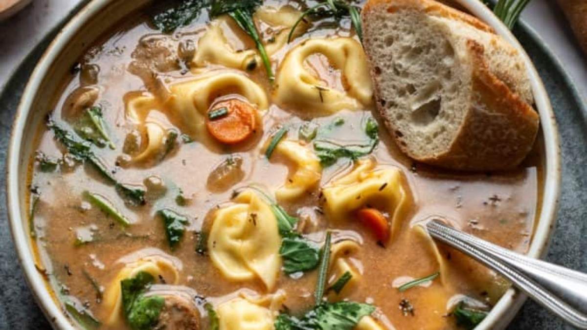 A shared bowl of round up tortellini soup with bread and spinach.