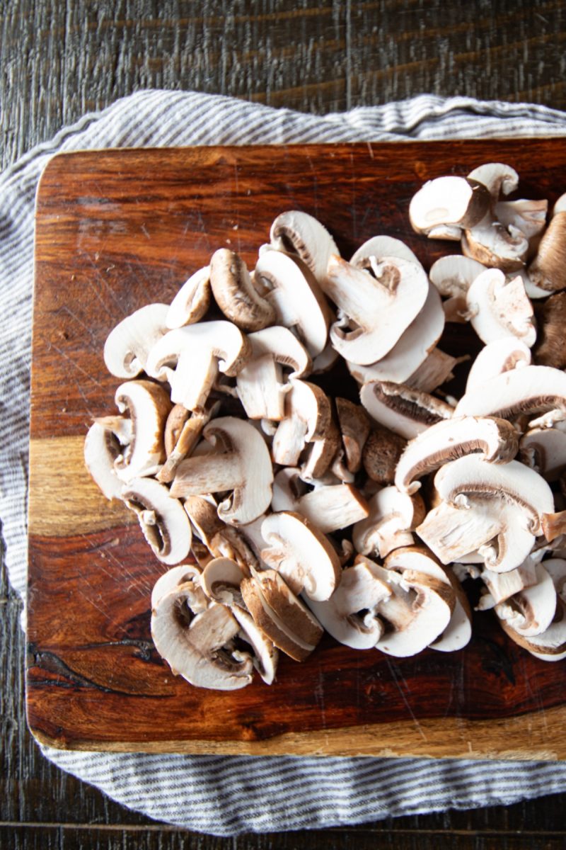 A wooden cutting board with raw sliced mushrooms on it.