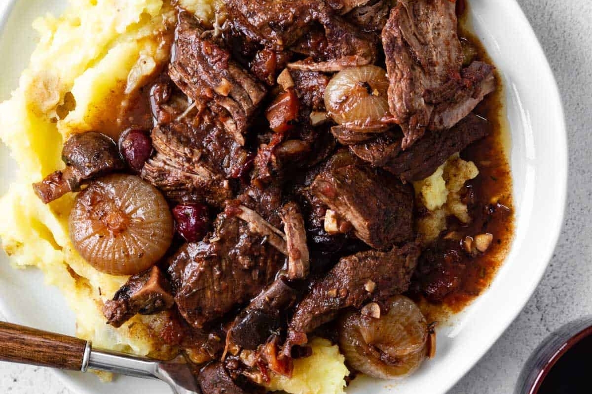 A hearty winter recipe consisting of beef served with a side of creamy mashed potatoes. The dish can be enjoyed using a fork to savor each delicious bite.