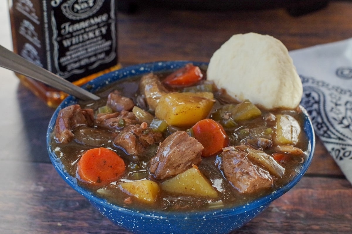 A slow cooker beef stew with dumplings and a bottle of whiskey.