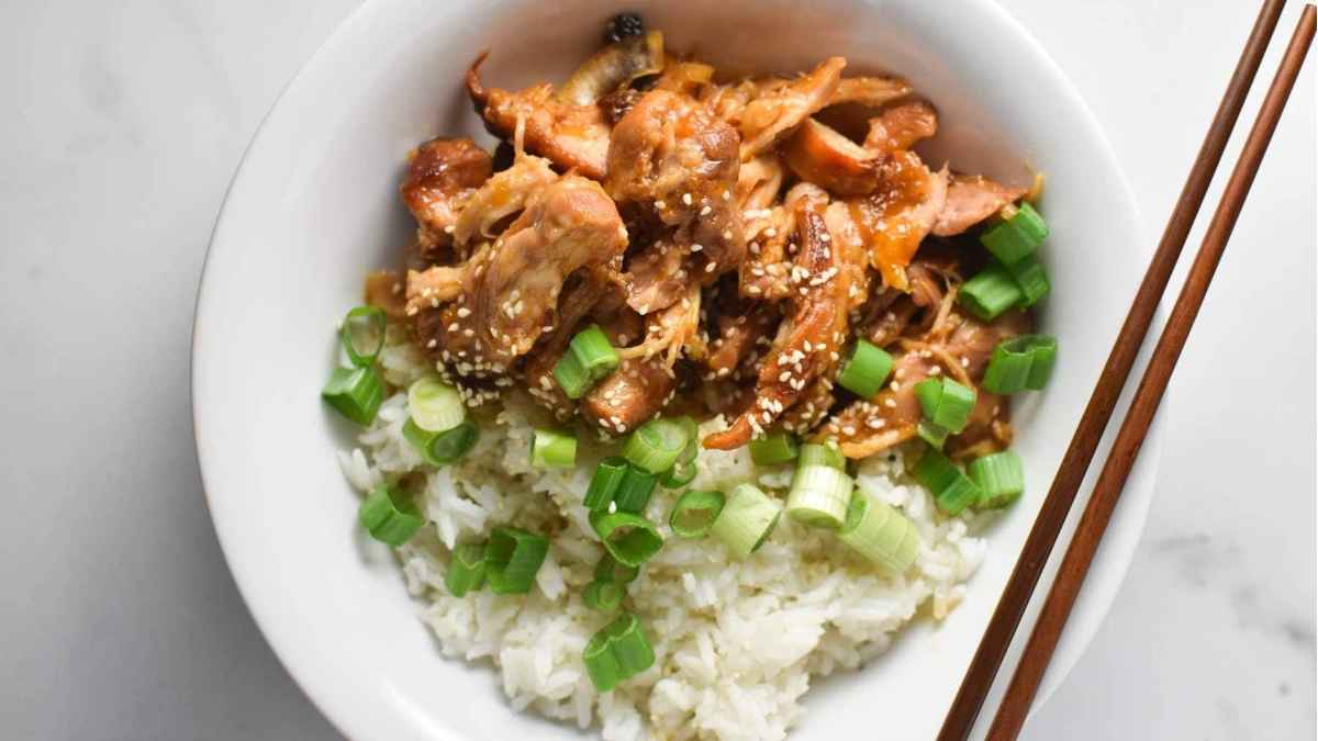 A slow cooker dinner of tender chicken served on a bed of fluffy rice, enjoyed with chopsticks.