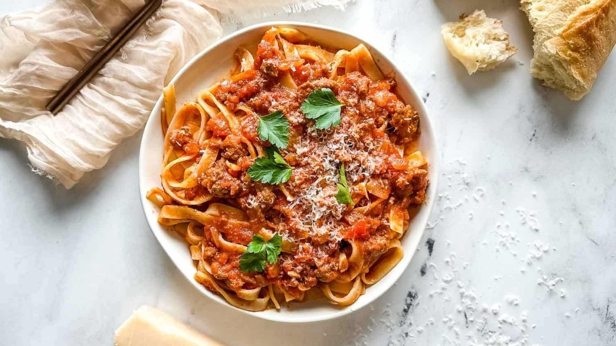 A romantic main dish perfect for Valentine's Day, indulge in a delicious bowl of pasta with meat sauce accompanied by warm bread.