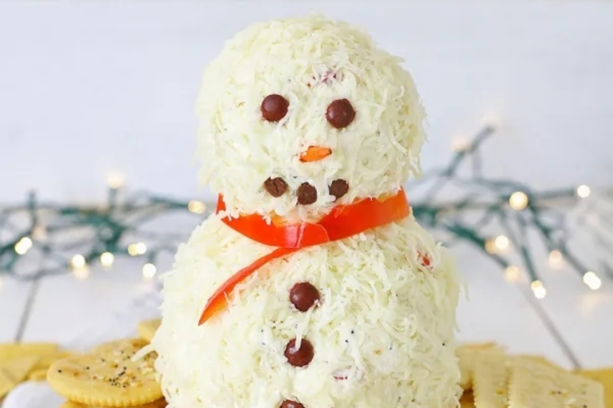 A Cheesy Christmas appetizer of a snowman made of cheese and crackers on a plate.