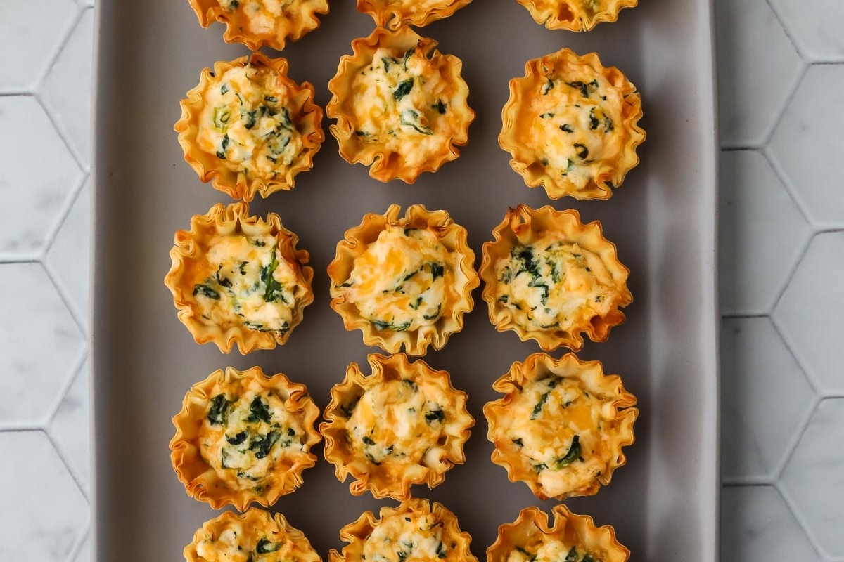 48 Easy Bite-Sized Appetizers Party Guests Will Love 26 Bite Sized cheesy spinach mini quiches on a tray.