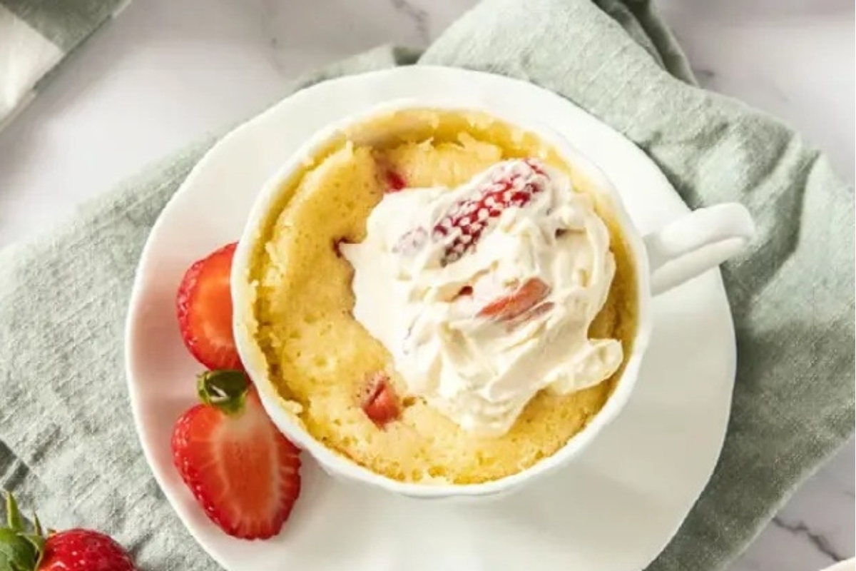 A delicious mug cake recipe for strawberry lovers topped with whipped cream and fresh strawberries.