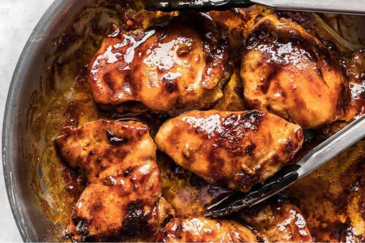 Bbq chicken in a skillet with two forks, using Chicken Thighs.