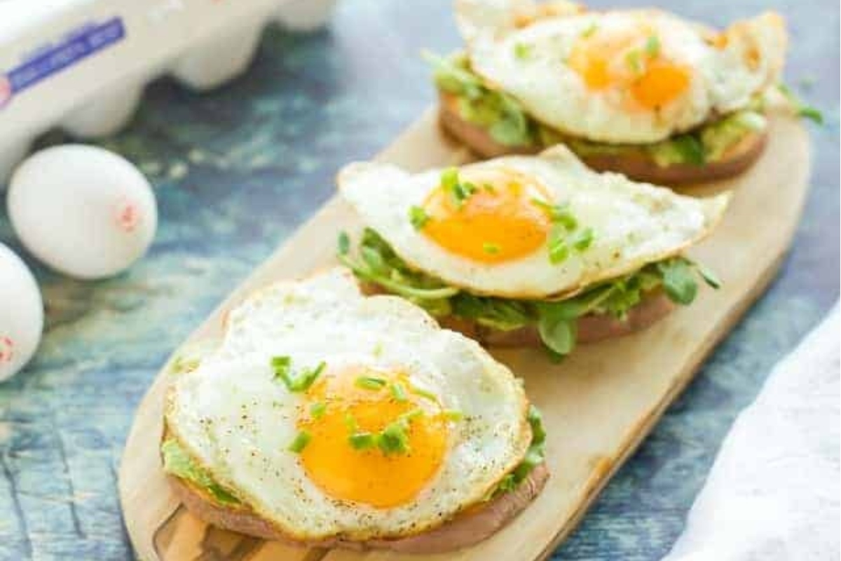 vocado toast with eggs on a wooden cutting board.
