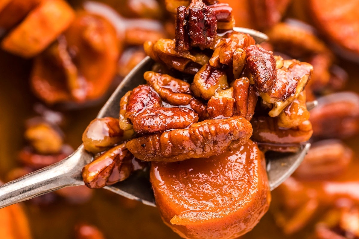 A delectable side dish for Christmas, featuring a spoon full of caramelized sweet potatoes and pecans.