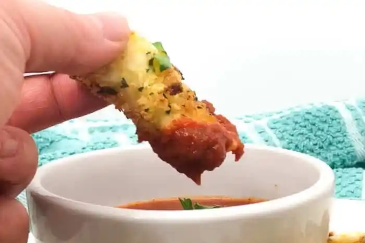 48 Easy Bite-Sized Appetizers Party Guests Will Love 42 A person enjoying bite-sized breadsticks dipped into a bowl of tomato sauce during game day.