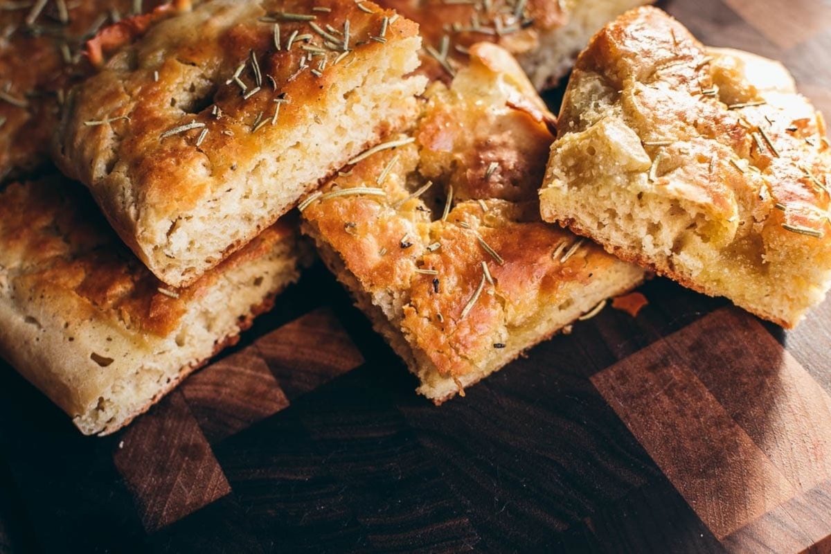 A slice of bread with sprigs of rosemary, perfect for homemade focaccia recipes, on a cutting board.