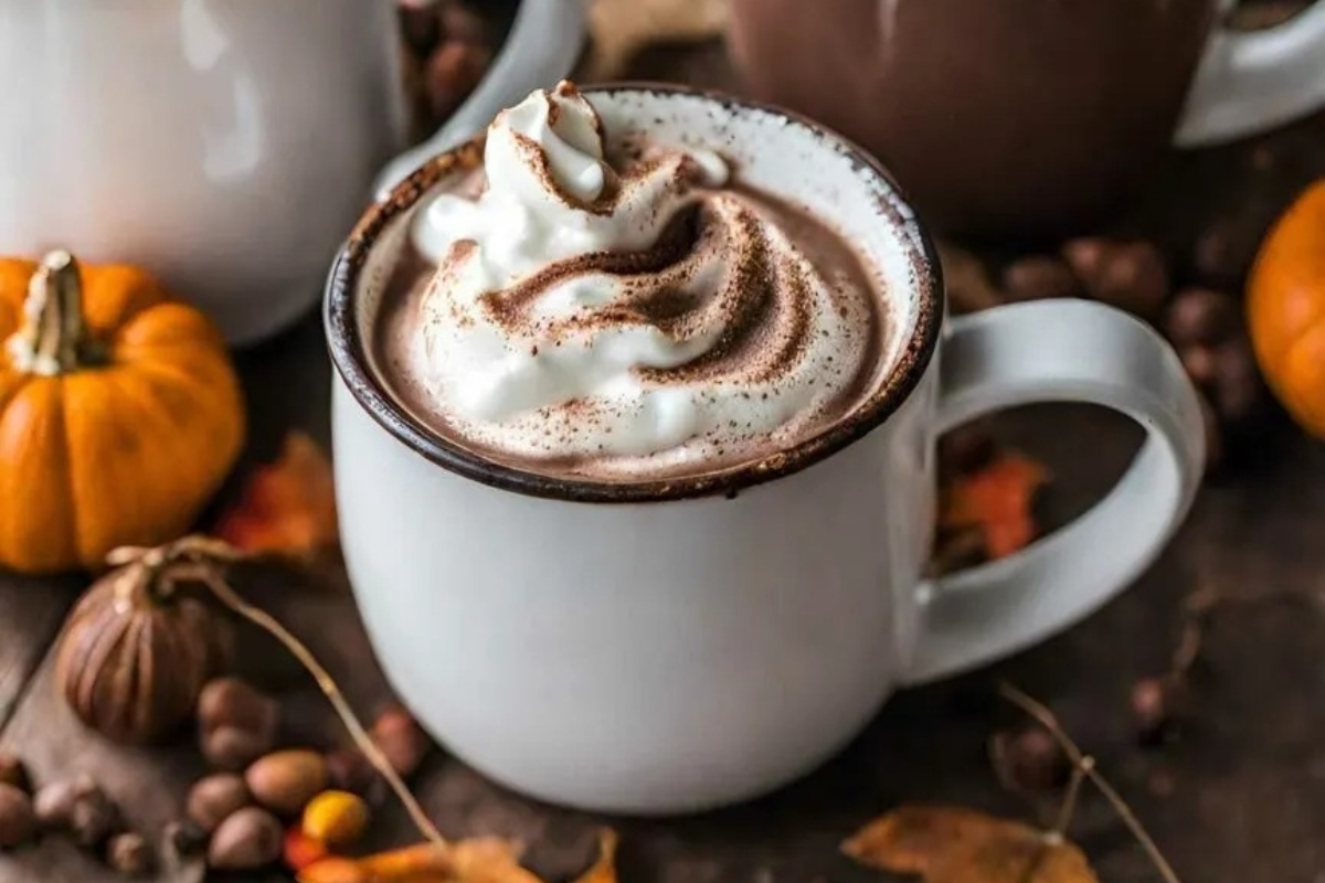 Three mugs of hot cocoa with whipped cream and pumpkins.