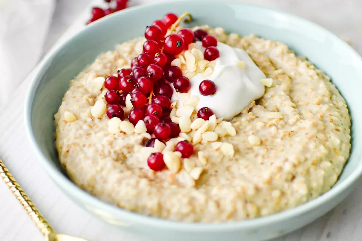 A healthy breakfast bowl of oatmeal with cranberries and whipped cream.