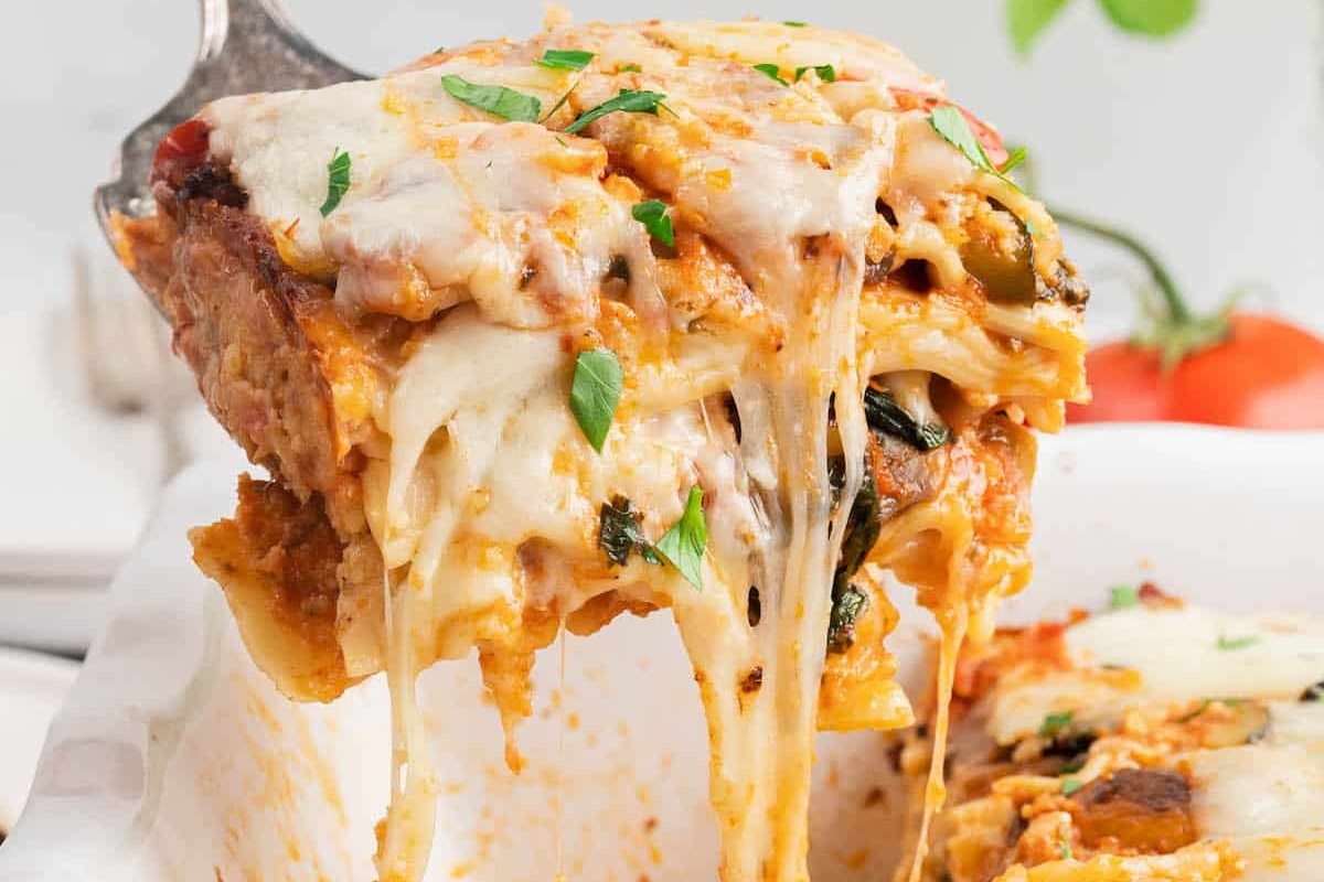 A vegetable-loaded lasagna being gracefully lifted out of a casserole dish.