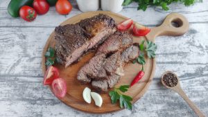 Air fryer steak on a wooden cutting board with tomatoes and herbs.