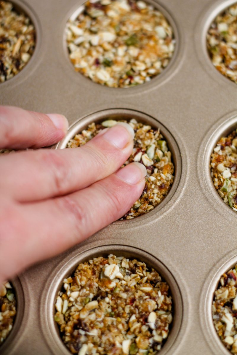 A person recreating an Aussie Bites copycat recipe by adding granola to a muffin tin.